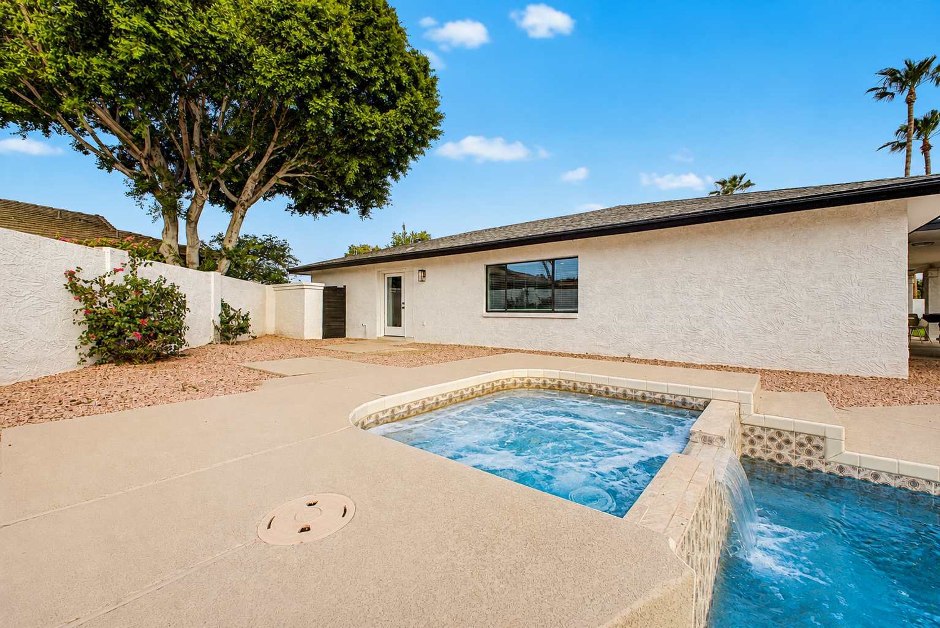 A residential property with a swimming pool, a covered patio, and a white exterior wall.