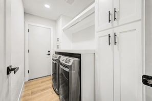 A narrow hallway with a white door at the end, a washing machine, and a built-in oven. - NEW The Fairmont Kierland Pool Spa Daybeds (Scottsdale)