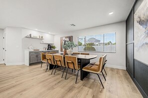 A modern kitchen with white cabinets, a dining area with a wooden table and chairs, and a large window with blinds. - NEW The Fairmont Kierland Pool Spa Daybeds (Scottsdale)