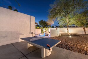 An outdoor ping pong table with a net, surrounded by a concrete wall and a tree. - The Brexton Luxe Scottsdale Resort-style Oasis (Scottsdale)