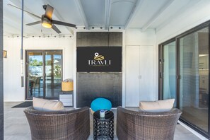 A modern outdoor seating area with wicker furniture, a ceiling fan, and a logo for TRAVLI Hospitality Co. - The Brexton Luxe Scottsdale Resort-style Oasis (Scottsdale)
