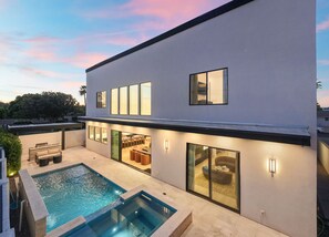 Ein modernes, zweistöckiges Haus mit Swimmingpool, Sitzgelegenheiten im Freien und großen Fenstern.