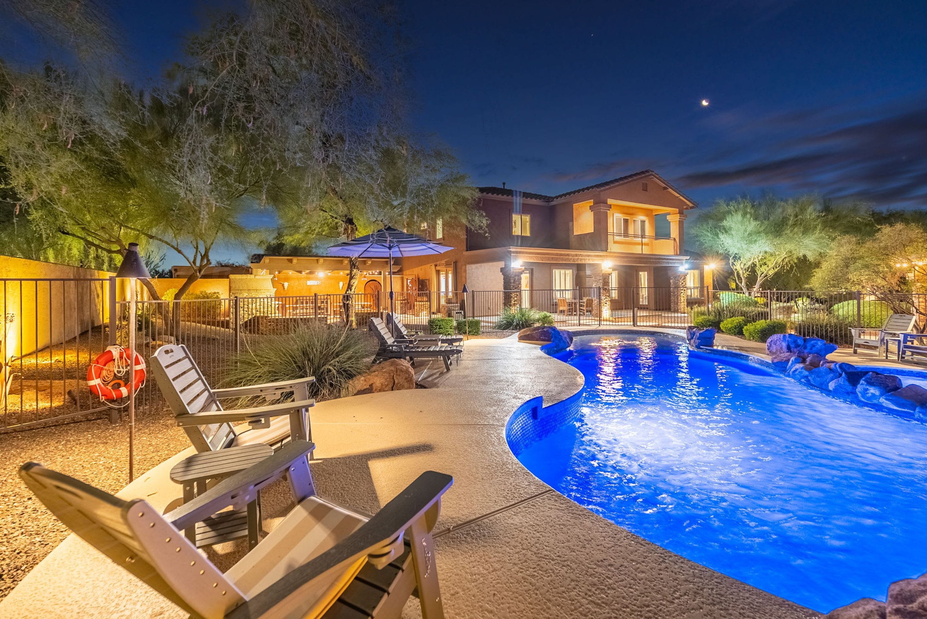 A residential property with a swimming pool, outdoor seating, and a well-lit patio area.