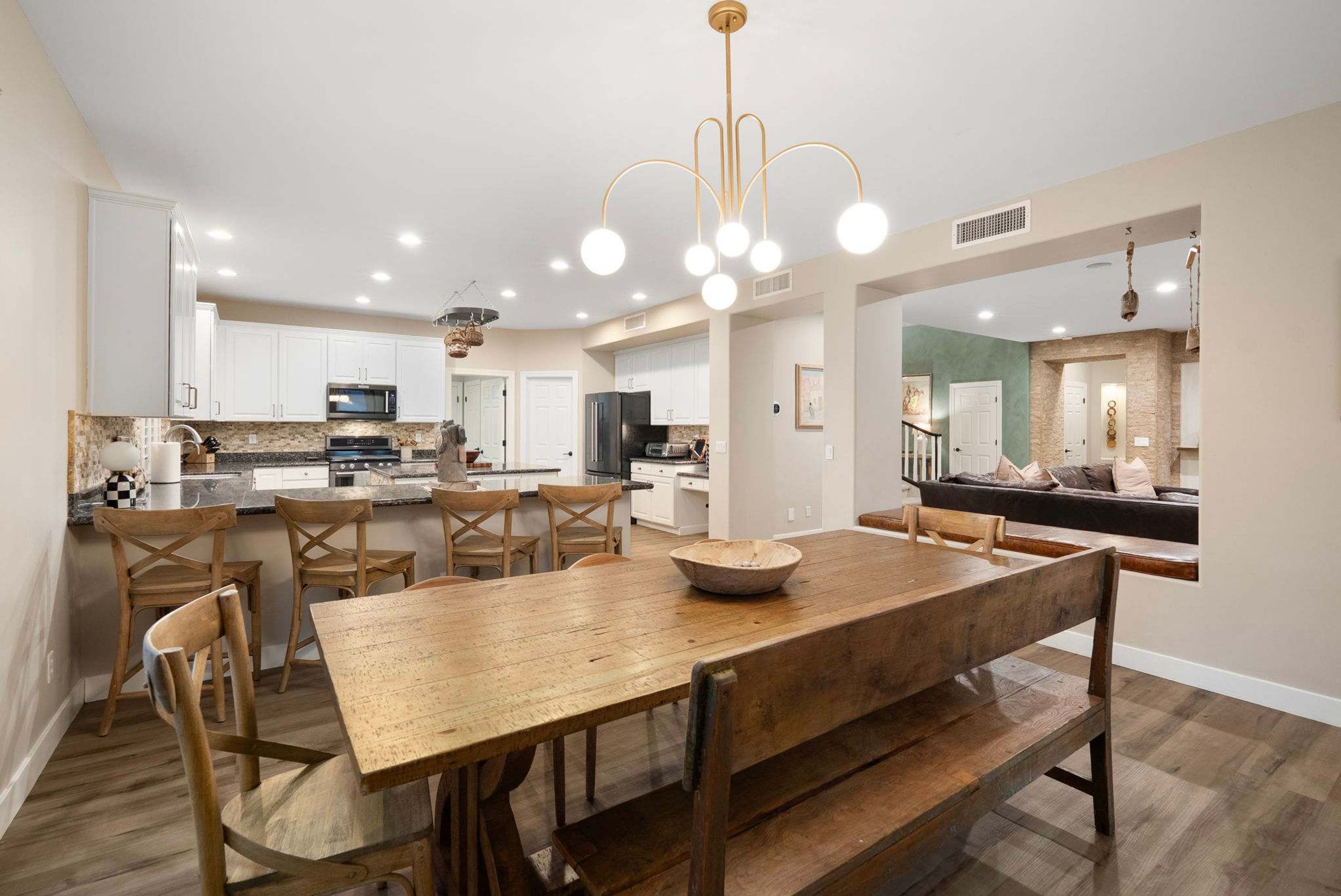A spacious kitchen with white cabinets, a dining area with a wooden table and chairs, and a modern chandelier.