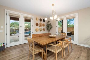 A dining area with a wooden table and chairs, a chandelier, and a wall with various hats. - NEW Lone Mtn Estate Resort-style Oasis Sleeps 14 (Cave Creek)
