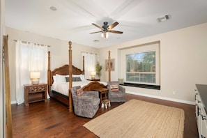 A bedroom with a four-poster bed, two armchairs, a large window with blinds, a ceiling fan, and a wooden floor. - NEW Lone Mtn Estate Resort-style Oasis Sleeps 14 (Cave Creek)