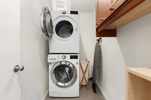 A compact laundry room with two stacked washing machines, a drying rack, and a wooden cabinet. - NEW Desert Bloom Pool Spa Game Room (Scottsdale)