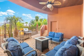 Eine überdachte Terrasse im Freien mit Grill, blau gepolsterten Sitzgelegenheiten und einem Deckenventilator.