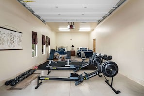 Ein Heimfitnessraum mit Trainingsgeräten, einem Bett und einem Fenster mit Vorhängen.