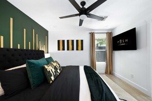 Ein modernes Schlafzimmer mit einer gepolsterten Kopfteil, einem Bett mit schwarz-weißer Bettwäsche, dekorativen Kissen, einem Deckenventilator und Kunstwerken an der Wand.