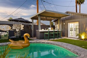 Un jardin avec une piscine, un espace salon extérieur et une fresque murale.