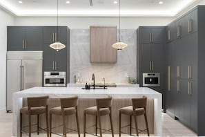 A modern kitchen with dark cabinets, stainless steel appliances, a central island with bar stools, and pendant lighting. - Mariposa Social Luxe Old Town Villa (Scottsdale)