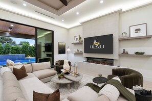 Ein modernes Wohnzimmer mit großem Flachbildfernseher, Kamin und Blick auf einen Pool.