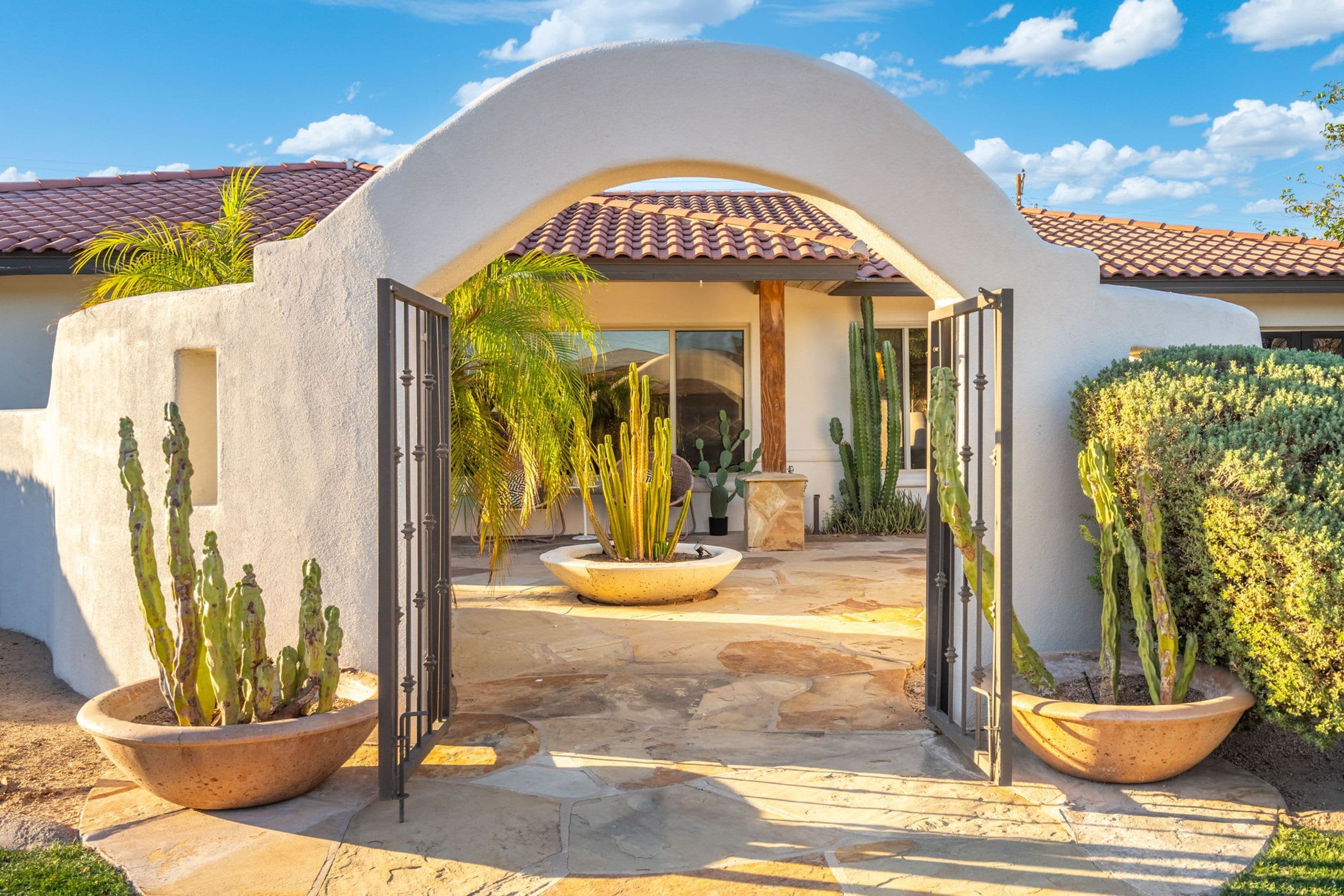 Une entrée de maison avec une façade en stuc blanc, un toit en tuiles et un chemin pavé menant à la porte.