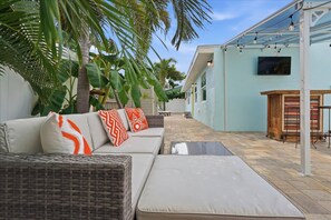 Ein sonniger Außenbereich mit einer Sitzecke, einer Couch, Kissen und einem Tisch.