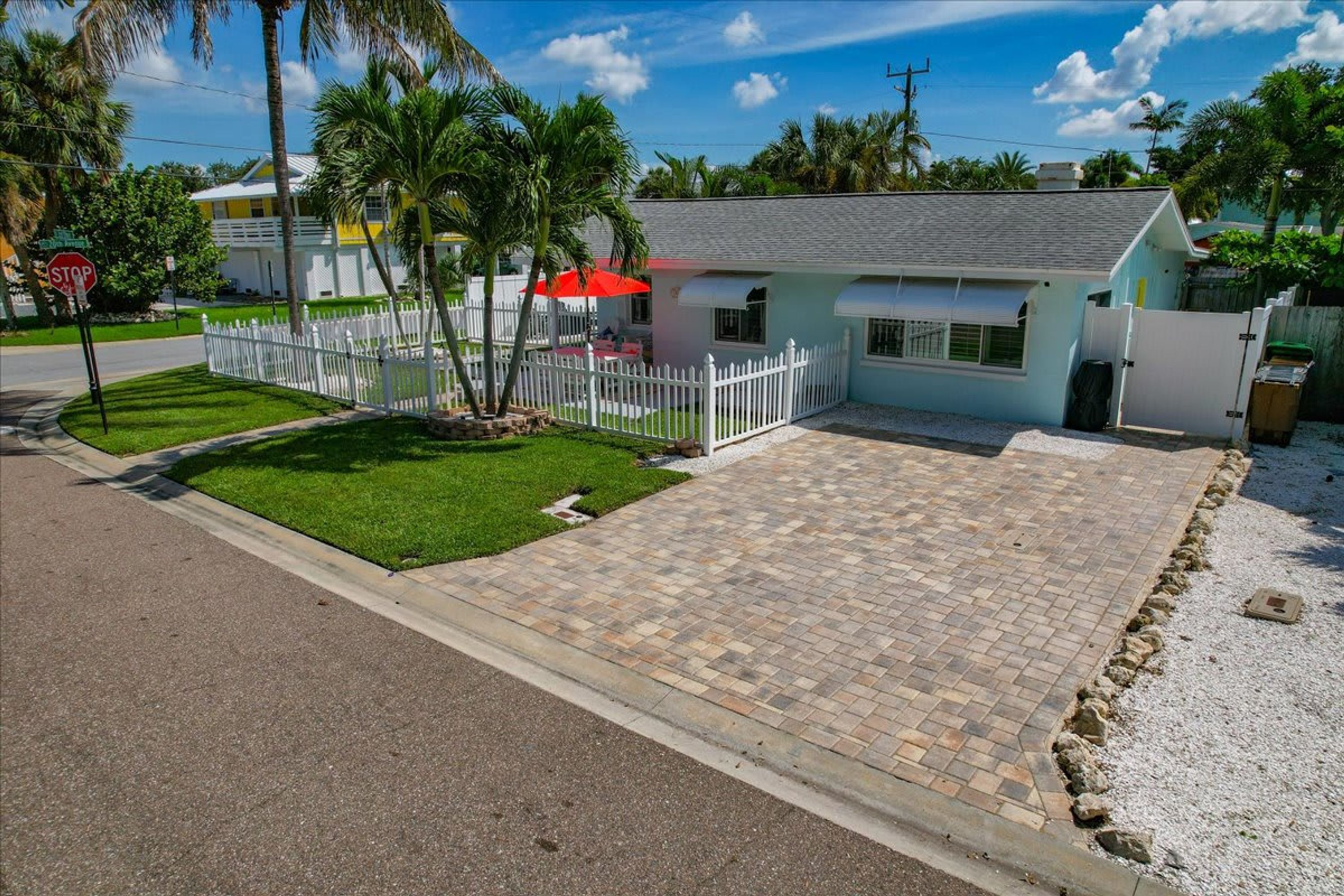 A residential property with a paved driveway, a white picket fence, and a small lawn.