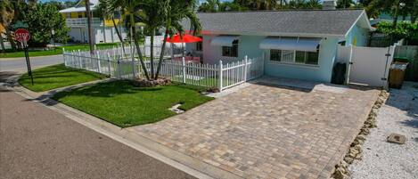 A residential property with a paved driveway, a white picket fence, and a small lawn.
