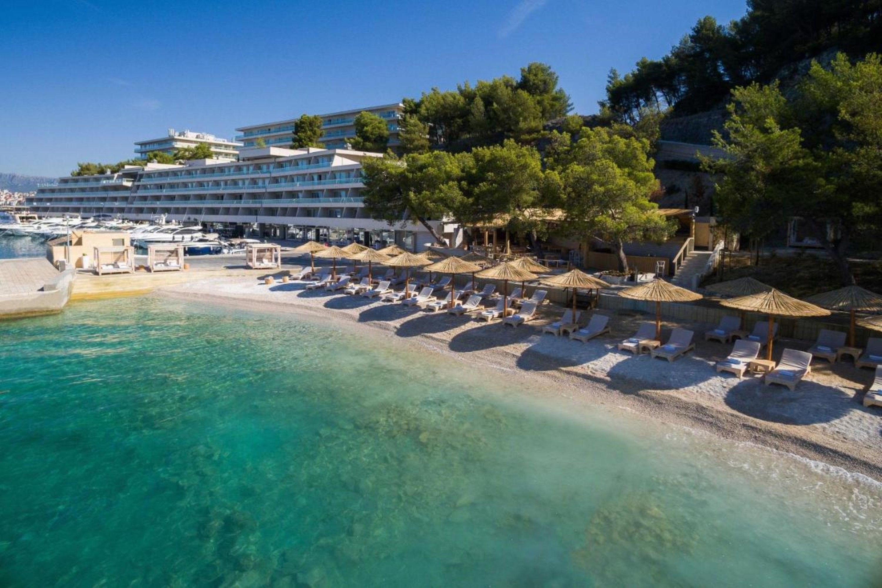 Un hotel frente a la playa con piscina, tumbonas y sombrillas.