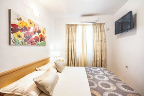 A hotel room with a bed, a painting, curtains, a TV, and an air conditioning unit. - A8 - Apartment with terrace and the sea view, 4 min walk to the beach (Žrnovnica)
