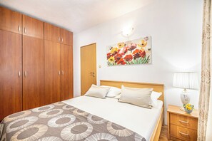 Een slaapkamer met een bed, een houten garderobe, een bloemschilderij, een nachtkastje en een lamp.