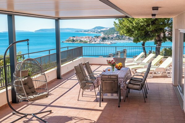 Een balkon met een tafel, stoelen en een hangstoel, met uitzicht op de kust.