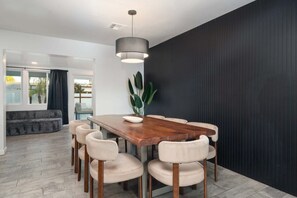 A modern dining area with a wooden table and six chairs, a hanging light fixture, and a large plant. - NEW The Tipsy Cactus Old Town Oasis Pool Bar Putt (Scottsdale)