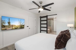 Een hotelkamer met een bed, een plafondventilator, een schuifdeur naar een badkamer en een aan de muur bevestigde televisie.