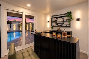 A modern kitchen with a bar area, a pool, and a sliding glass door leading to an outdoor patio. - NEW The Tipsy Cactus Old Town Oasis Pool Bar Putt (Scottsdale)