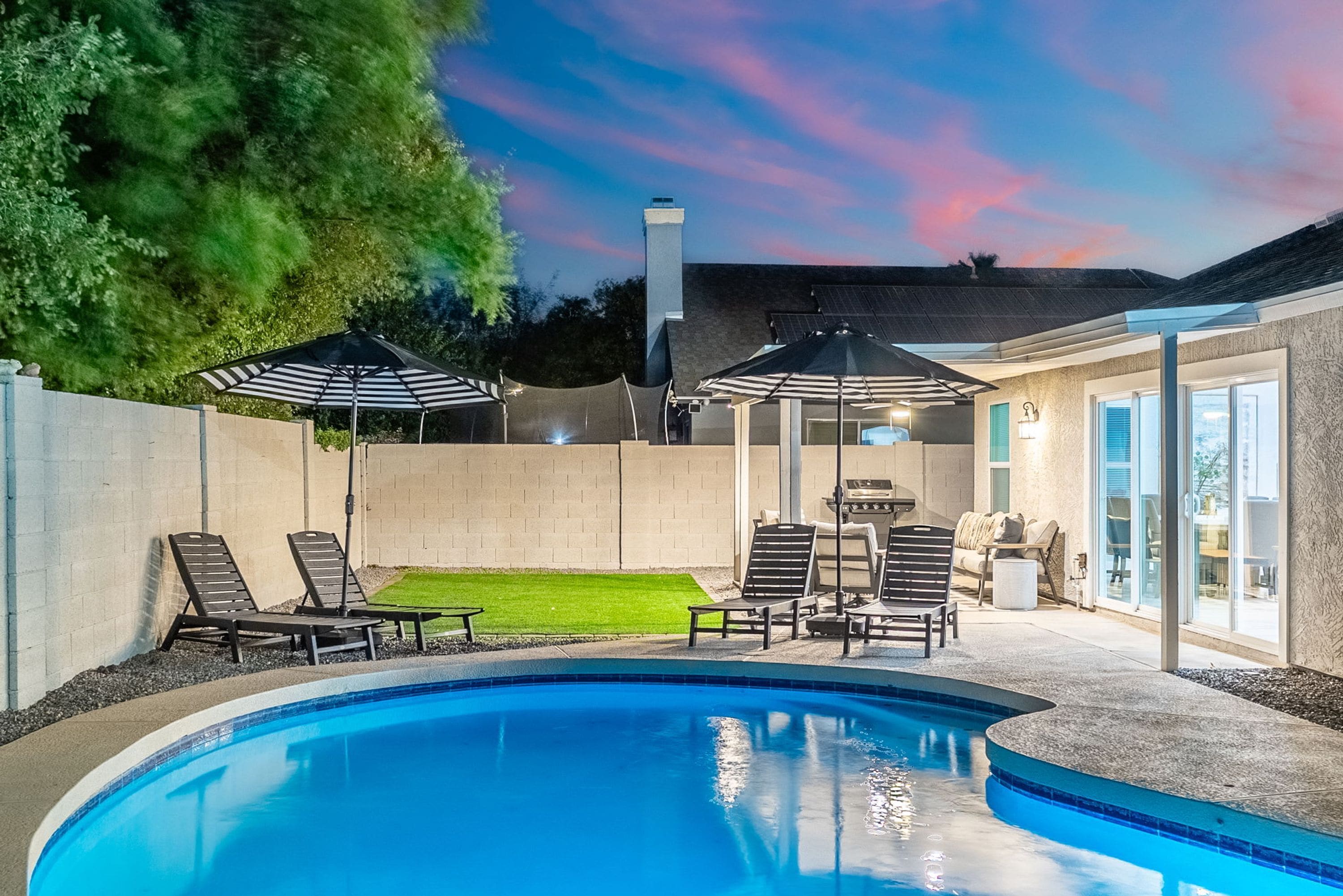 A backyard with a swimming pool, lounge chairs, and umbrellas.