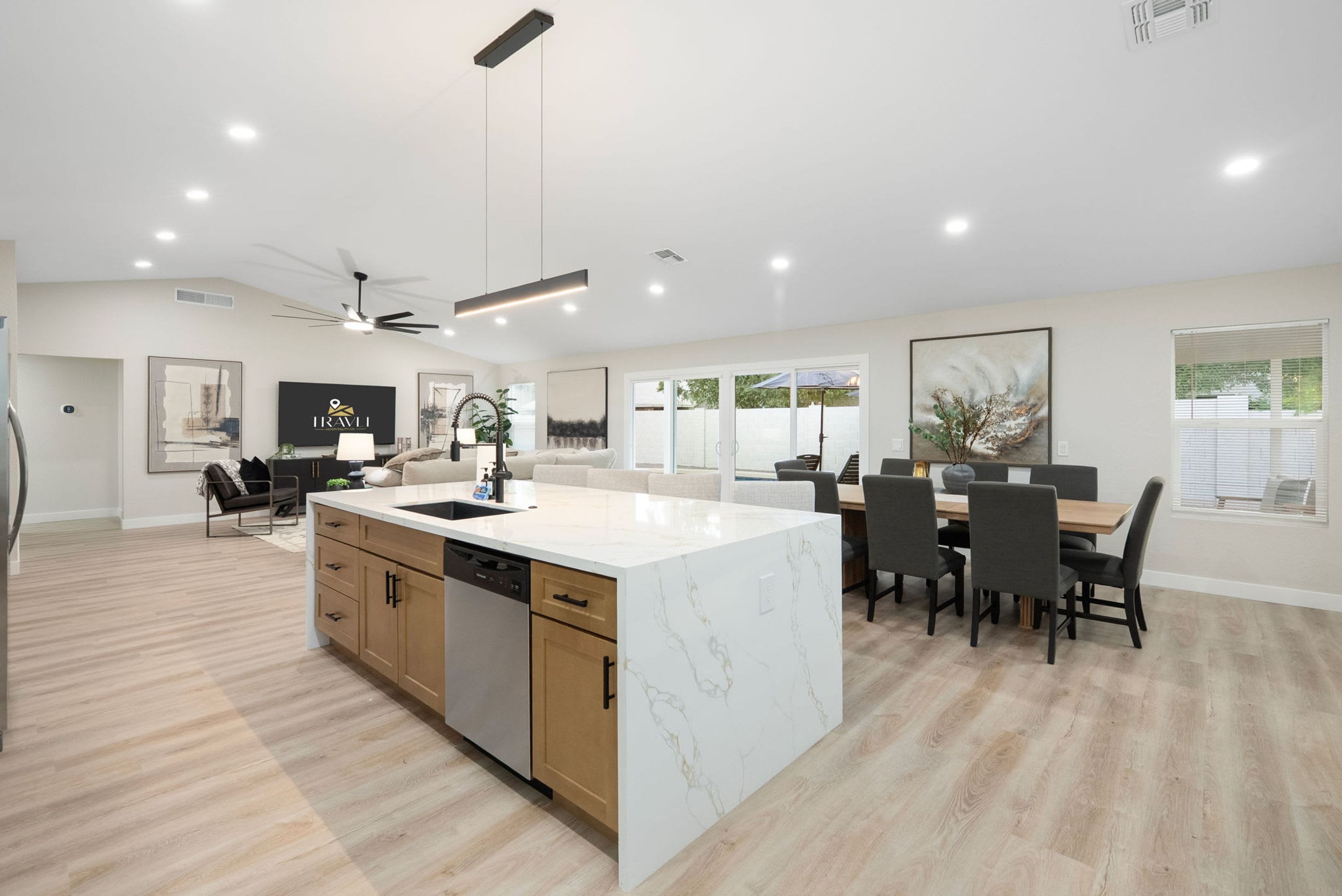 A modern kitchen with a marble island, wooden cabinets, and a dining area with a table and chairs.