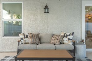Ein beiges Sofa mit gemusterten Kissen, ein Holztisch und eine Wand mit Struktur, ergänzt durch einen Laternenleuchter.