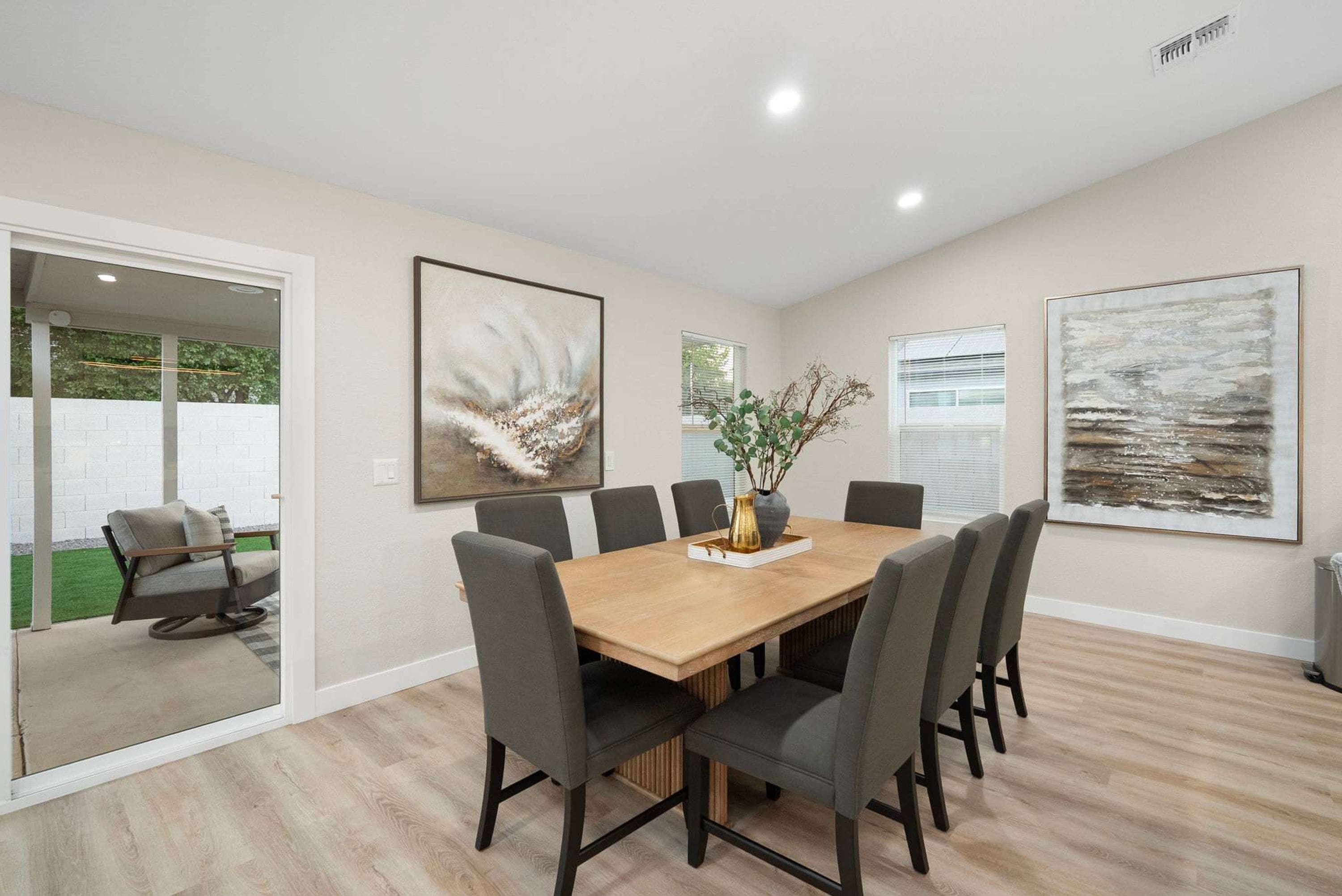 Un coin repas avec une table en bois, six chaises et deux tableaux abstraits accrochés aux murs.