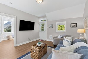 A modern living room with a flat-screen TV, a grey sofa, a wicker coffee table, and a grey couch with blue cushions. - Seabrook All Decked Out | Hot Tub, Dog Friendly, Sleeps 9, Pool Access (Pacific Beach)