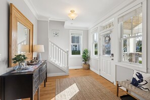 A hallway with a staircase, wooden floors, a black console table with a lamp, and a door with a window. - Seabrook All Decked Out | Hot Tub, Dog Friendly, Sleeps 9, Pool Access (Pacific Beach)