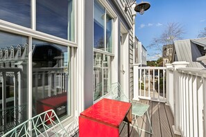 Eine Terrasse mit rotem Tisch und Stühlen, großen Fenstern und einem weißen Zaun.