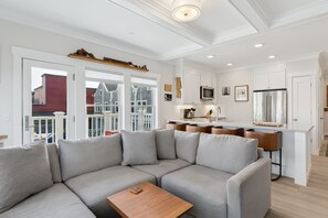 A modern living room with a sectional sofa, a wooden coffee table, and a kitchen area with white cabinetry and stainless steel appliances. - Seabrook Lumber Yard | Dog Friendly, Town Center, Pool Access, Sleeps 2 (Pacific Beach)