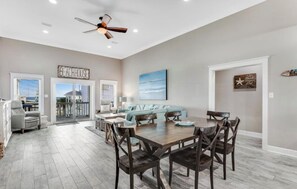 A spacious dining area with a high ceiling fan, a view of the beach through the sliding glass doors, and a cozy seating area with a light blue sofa. - New Listing! In Morgantown Pools/Pickleball (Gulf Shores)
