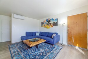 A living room with a blue sofa, a glass coffee table, a patterned rug, and a door. - Quaint & Cozy Hideaway! 15 Min to LAX (Los Angeles)