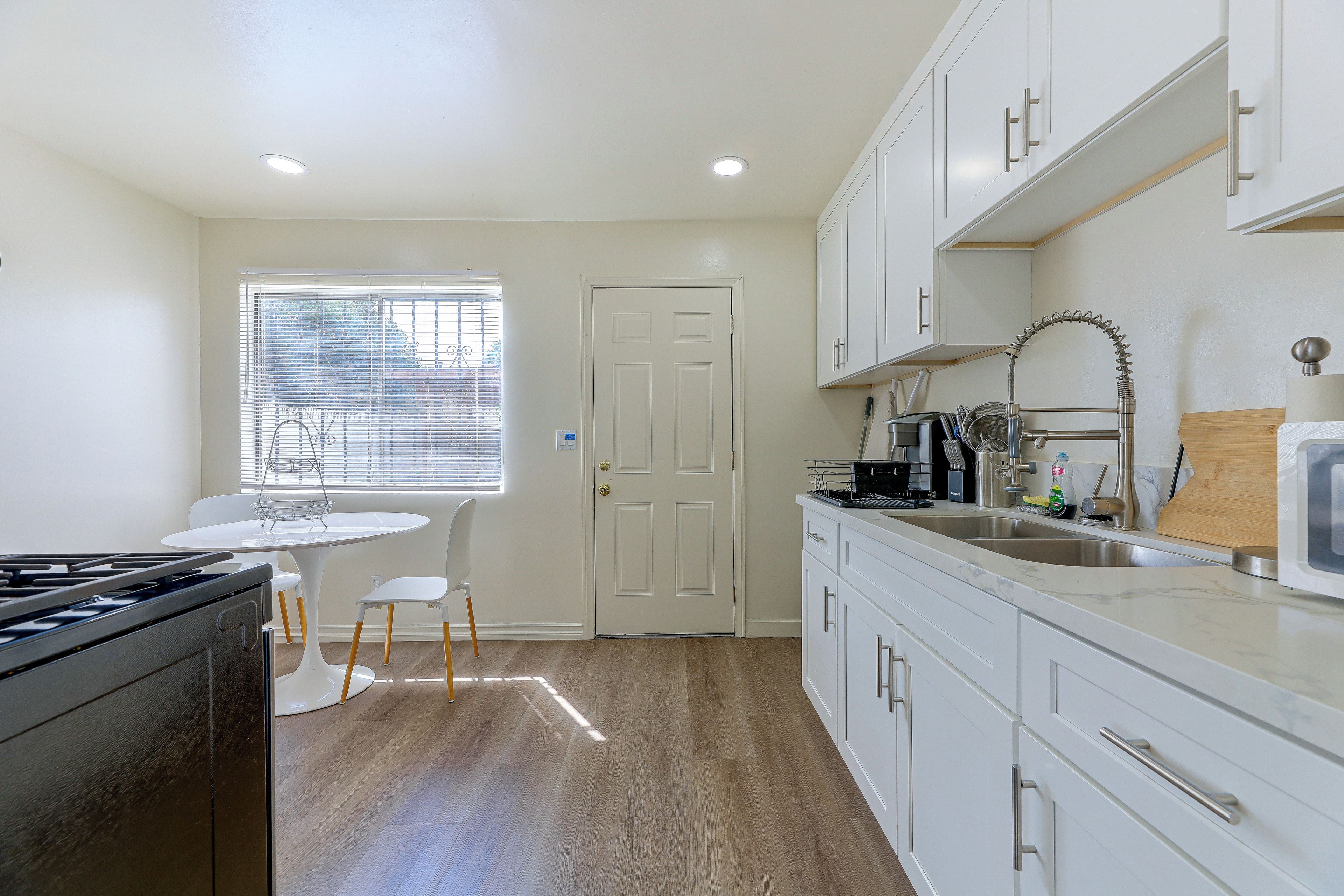 A modern kitchen with white cabinetry, a gas stove, a sink, and a window with blinds.