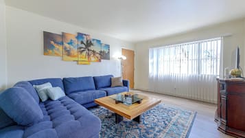 A living room with a sectional sofa, a coffee table, a patterned rug, and a large window with blinds.
