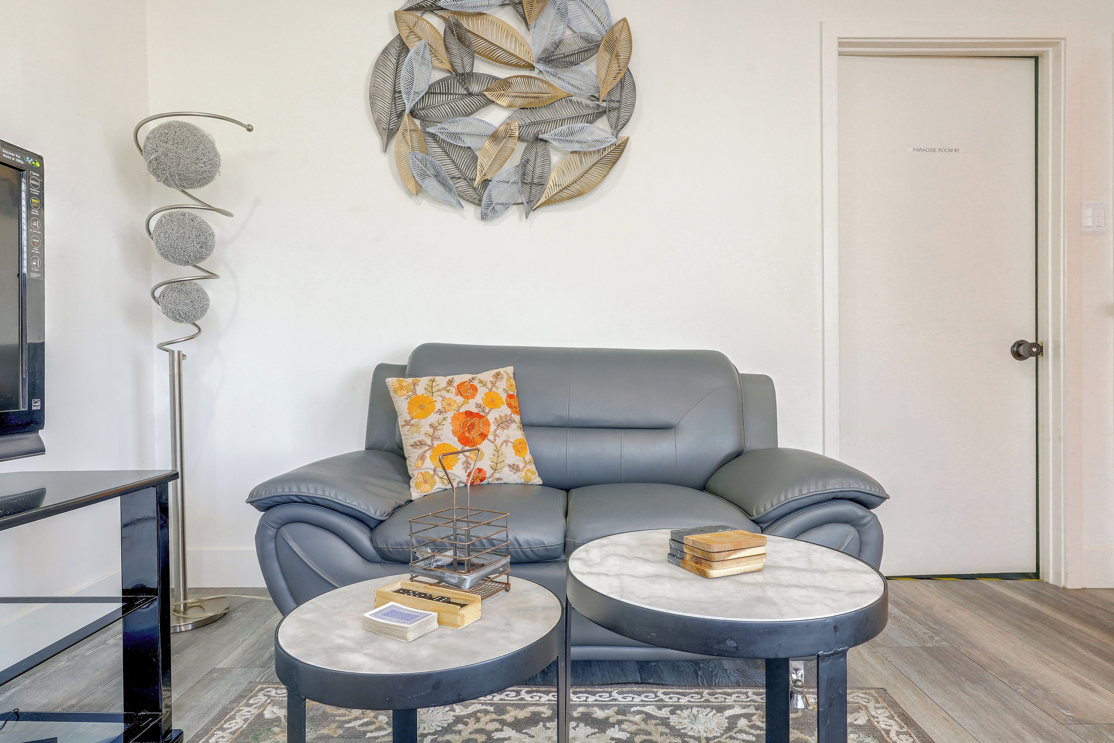 A modern living room with a grey sofa, a decorative wall piece, a flat-screen TV, and a coffee table with books.