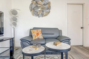 A modern living room with a grey sofa, a decorative wall piece, a flat-screen TV, and a coffee table with books. - LA Home w/ Porch, 3 Mi to Stadiums! (Los Angeles)