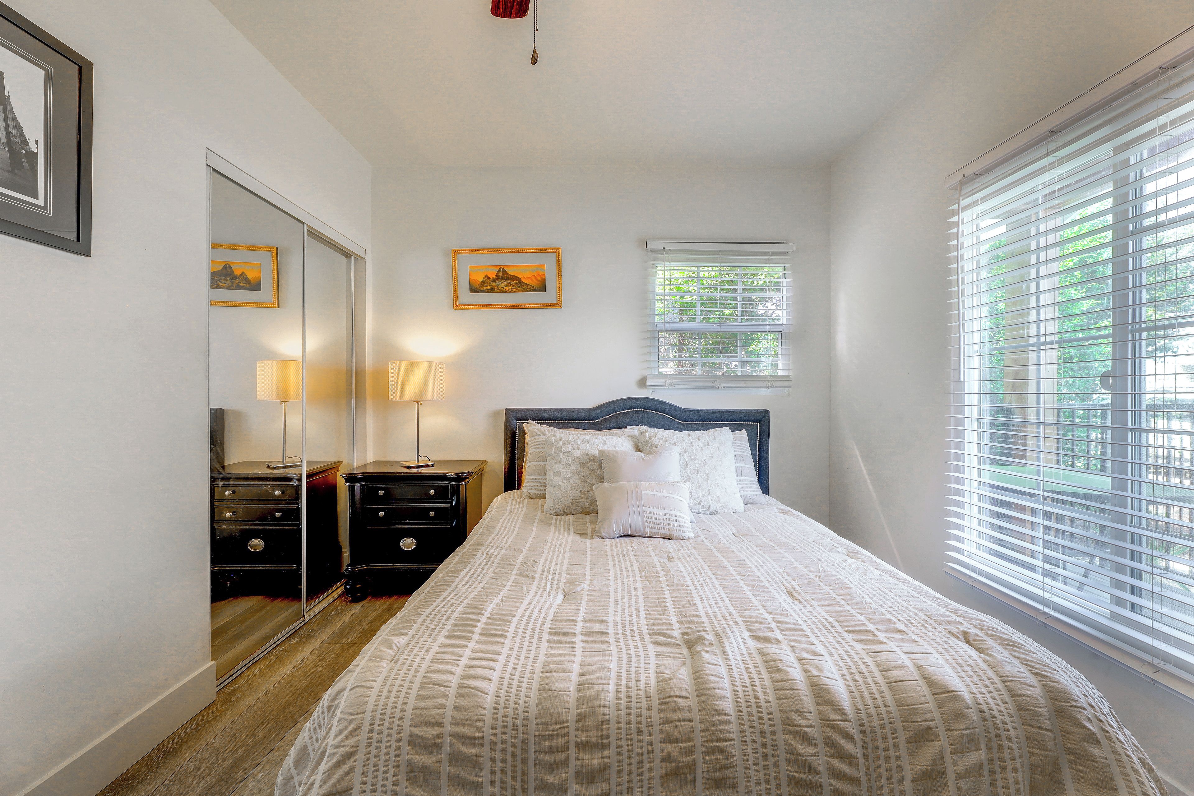 A bedroom with a bed, bedside tables, a mirror, and a window with blinds.