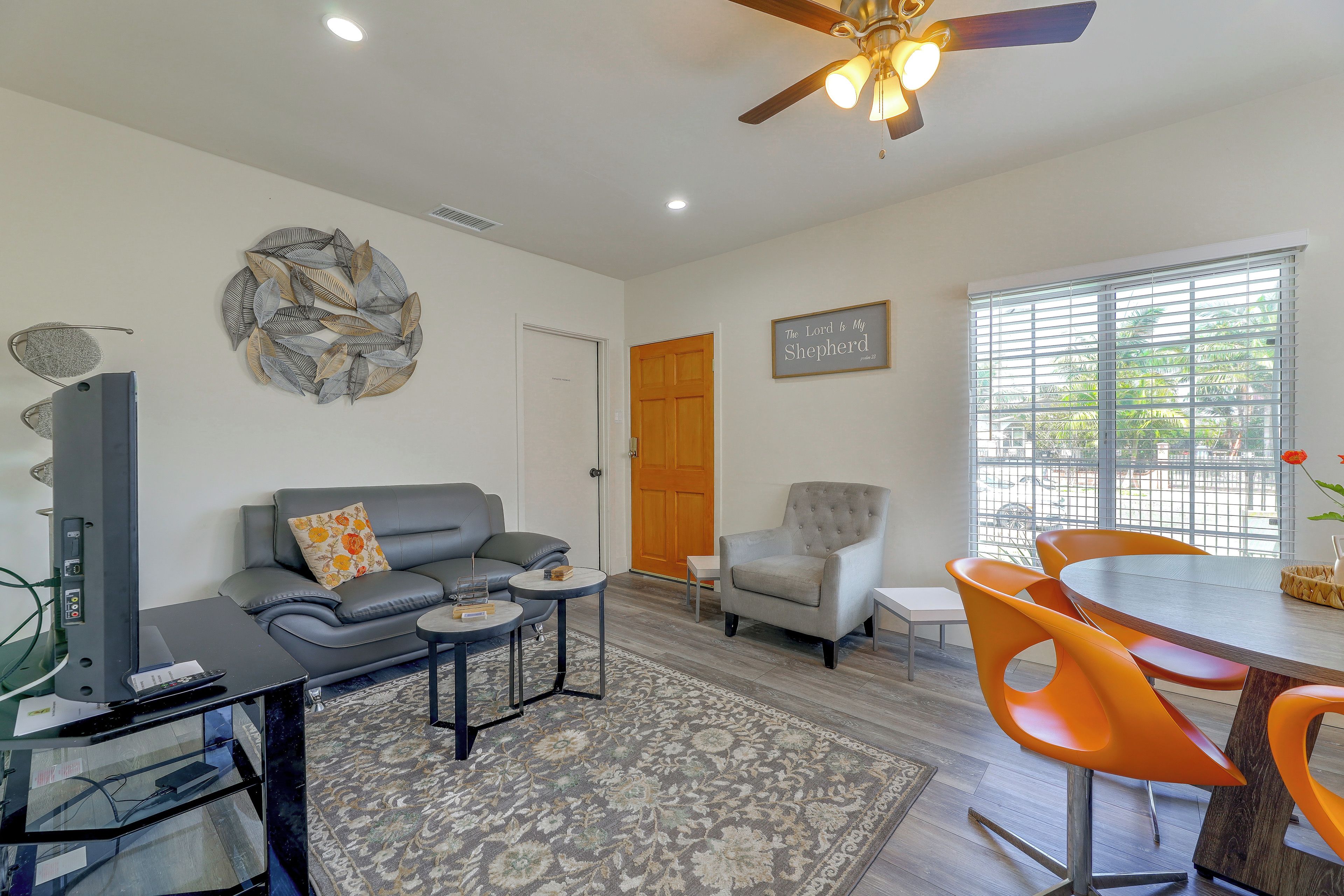 A living room with a grey sofa, a small round table, a grey armchair, and a dining area with orange chairs.