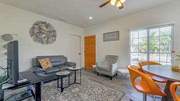 A living room with a grey sofa, a small round table, a grey armchair, and a dining area with orange chairs.