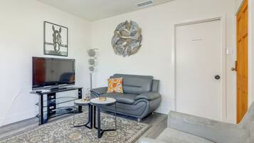A modern living room with a grey sofa, a flat-screen TV, a decorative wall piece, and a patterned rug.