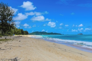 Ein Strand mit blauem Himmel, ruhigem Wasser und Bergen in der Ferne.