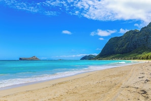A beach with clear turquoise water, sandy shore, and a mountain in the background. - Steps to Beach! Waimanalo Beach Cottages, Unit 10 (Waimanalo)