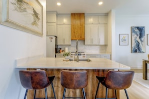 A modern kitchen with a large island, bar stools, and wooden accents. - 5 Mi to UF! Luxury 2-unit Combo w/ Hot Tub (Gainesville)
