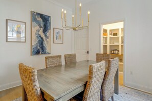 Ein Esszimmer mit Holztisch, Korbstühlen, einer Chandelierleuchtre und Kunstwerken an den Wänden.